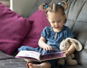 Cute toddler girl reading a book at home
